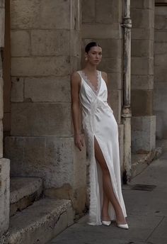 a woman in a white dress leaning against a wall