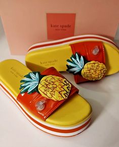 a pair of yellow shoes with pineapples on them are next to a pink box