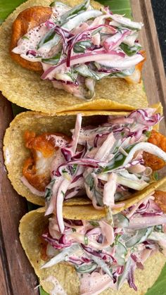 three tacos with meat, lettuce and sauce on them sitting on a wooden tray