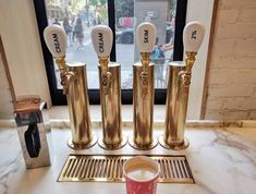 three golden spoons and two cups on a marble counter top in front of a window