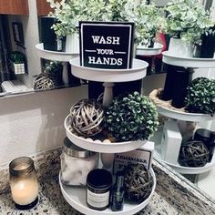 three tiered trays holding plants and candles on a bathroom counter with a sign that says wash your hands