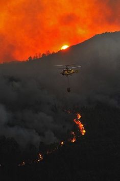 a helicopter flying over a forest filled with fire