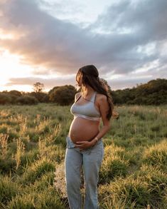 a pregnant woman standing in a field at sunset