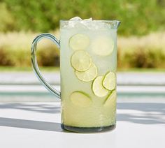 a pitcher filled with ice and lemon slices on top of a white table next to grass