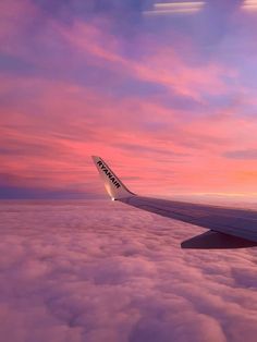 the wing of an airplane as it flies above the clouds at sunset or dawn with pink and purple hues