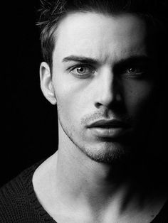 a black and white photo of a man with dark hair looking at the camera while wearing a sweater