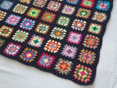 a crocheted blanket is laying on top of a white bed sheet with multicolored squares