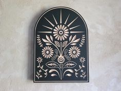 a black and white wall hanging with flowers on it's side, in front of a stucco wall