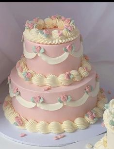 a three tiered cake with pink and white frosting flowers on it, next to two smaller cakes