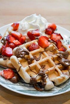 a waffle topped with strawberries and chocolate sauce on a plate next to whipped cream