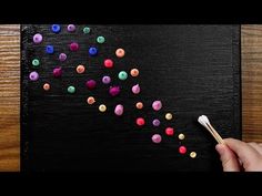 a person is painting with colored crayons on a black piece of wood and holding a paintbrush