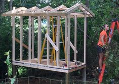 a man standing on top of a wooden structure in the woods next to a ladder