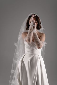 a woman in a white wedding dress with her hands on her face while wearing a veil