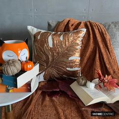 an orange and white pillow on top of a bed next to a book, pumpkins and other items