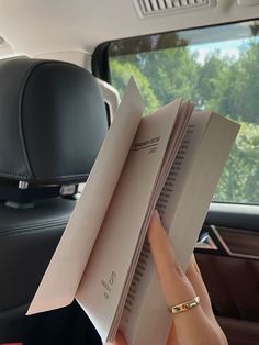 a person holding two books in their hand while sitting in the back seat of a car