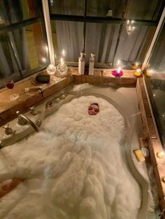 a bathtub filled with lots of white foam next to candles and bottles on the counter