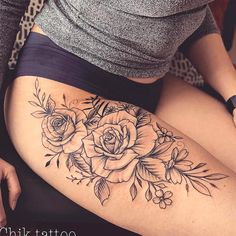 a woman is sitting on the floor with her thigh covered in roses and leaves tattoo