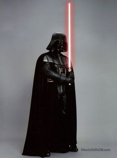 darth vader standing in front of a grey background with his lights on and holding the light saber