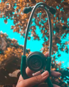 a hand holding a stethoscope in front of a tree with blue sky