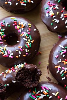 several chocolate donuts with sprinkles on a wooden surface, ready to be eaten