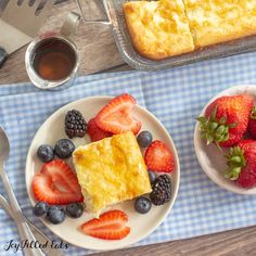 two plates with slices of cake and strawberries on them next to a fork, knife and spoon