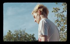 a man with blonde hair standing in front of trees