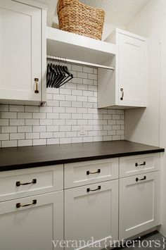 a kitchen with white cabinets and black counter tops in front of a basket hanging on the wall