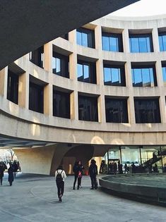 people are walking around in front of a circular building with many windows on the sides