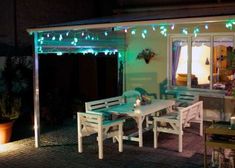 an outdoor dining area is lit up with green and white string lights, while the patio has been decorated with potted plants