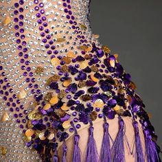 the back of a woman's dress with purple beads and tassels on it