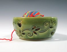 a green bowl with a ball of yarn in the center and a red string attached to it