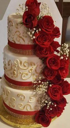 a three tiered wedding cake with red roses and baby's breath on top