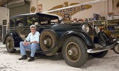 an old man sitting in front of a vintage car