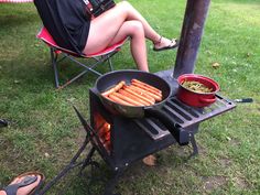 a woman sitting in a chair next to a grill with hot dogs on it