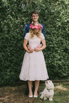 a man and woman standing next to each other in front of a hedge with a dog