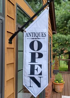 an open sign hanging from the side of a house next to a potted plant