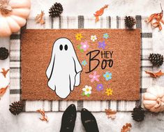 a door mat with a cartoon ghost on it and the words hey boo spelled in black