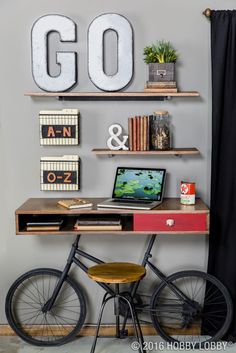 a desk with a laptop and some books on it in front of a wall mounted letter