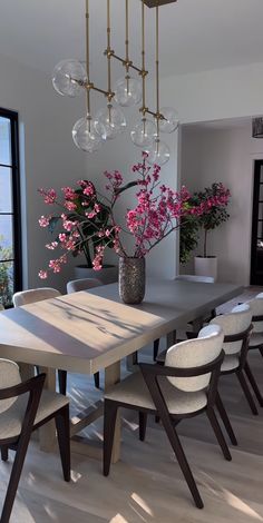 a dining room table with white chairs and a large vase filled with flowers on it