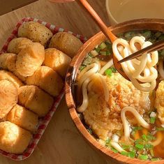 a wooden table topped with bowls filled with soup and veggies next to rolls