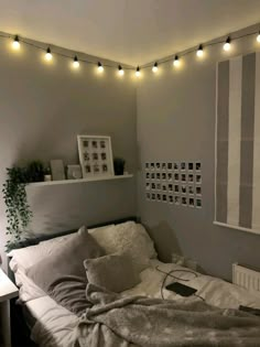 an unmade bed in a small room with lights on the ceiling and pictures hanging above it