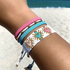 a close up of a person's arm with bracelets on it and the ocean in the background