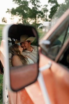 a man and woman are kissing in the back of a car while it's reflection is in the rear view mirror