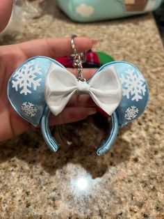 a person holding a mickey mouse ear keychain with snowflakes on it