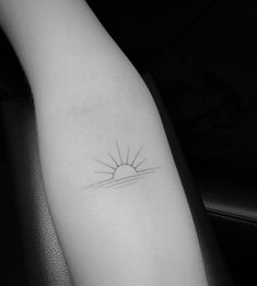 a black and white photo of a small sun tattoo on the left inner arm,