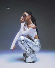 a woman sitting on the ground with her legs crossed, wearing shiny silver pants and white shirt