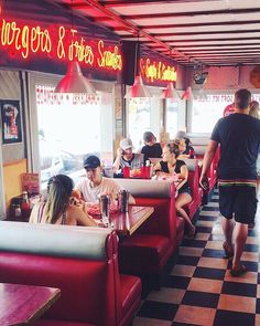 people sitting at booths in a restaurant with checkered flooring and neon signs above them