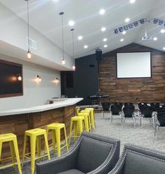 an empty room with yellow stools in front of a bar and projector screen