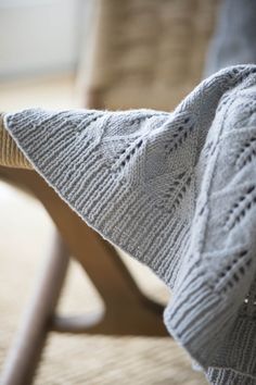 a white knitted blanket sitting on top of a wooden chair