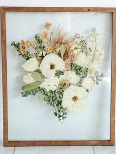 an arrangement of flowers in a wooden frame on the floor next to a white wall